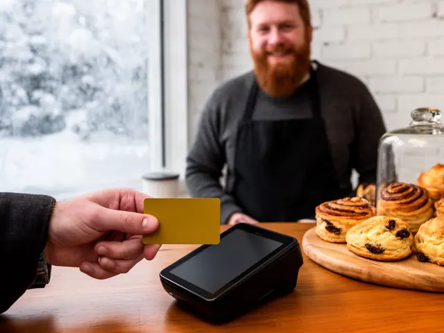 Customer tapping a yellow card on a countertop card terminal in a cozy bakery with the smiling owner behind